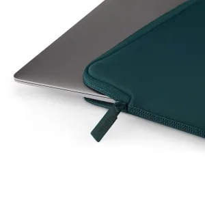Housse Pipetto Classic Fit en bleu sarcelle foncé, enveloppant partiellement un MacBook argenté, avec fermeture zippée