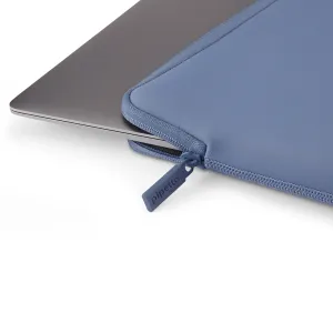 Housse Pipetto bleue pour MacBook, avec fermeture zippée, recouvrant partiellement un ordinateur portable argenté pour le protéger