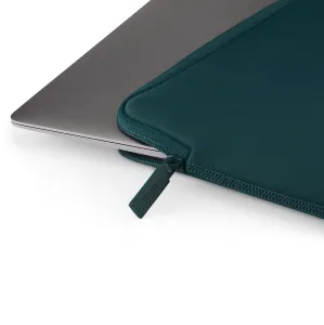 Pipetto Classic Fit MacBook apvalks tumši zilganzaļā tonī ar rāvējslēdzēja cilpiņu un polsterētu apmali, attēlots blakus sudraba klēpjdatoram